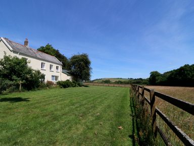 A house with grass lawn and wooden fence next to open field and trees at Marsh Cottage in North Molton