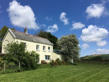A two-story cream house with a lawn and trees under a blue sky at Marsh Cottage in North Molton