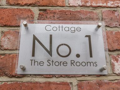 A metal sign on a brick wall reading Cottage No 1 The Store Rooms