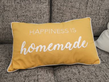 A yellow cushion with the words happiness is homemade on a gray sofa at The Store Rooms in Whitby