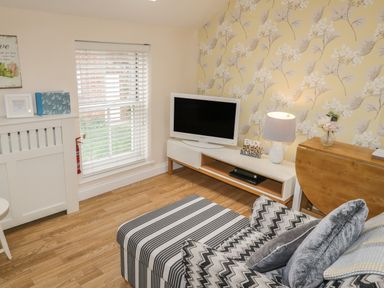 A living room with a striped chair a television on a stand and floral wallpaper at The Store Rooms in Whitby