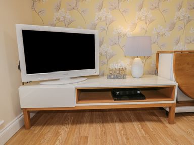 A television on a white and wooden stand with a lamp and decorative text on top at The Store Rooms in Whitby
