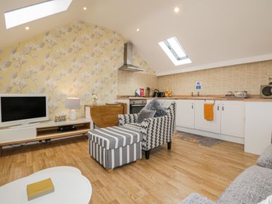A living area with a patterned armchair and ottoman a kitchen with white cabinets and skylights at The Store Rooms in Whitby