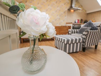 A glass vase with white flowers on a table in a living room with striped furniture at The Store Rooms in Whitby