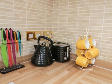A kitchen countertop with colorful knives in a stand black kettle black toaster and yellow mugs on a stand at The Store Rooms in Whitby