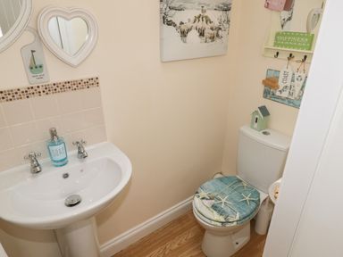 A small bathroom with a white sink and toilet and a toilet seat with starfish design at The Store Rooms in Whitby