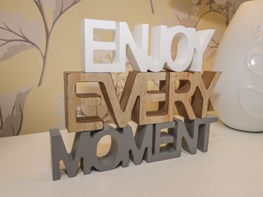 A decorative sign with the words enjoy every moment on a surface with floral wallpaper at The Store Rooms in Whitby