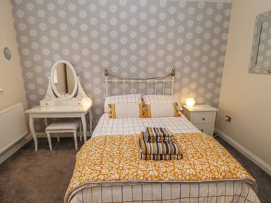 A bedroom with a bed with pillows and blankets a dressing table with a mirror and a stool and a bedside table with a lamp at The Store Rooms in Whitby