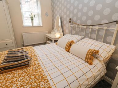 A bedroom with a bed with patterned bedding a bedside table with a mirror and lamp and a window with blinds at The Store Rooms in Whitby