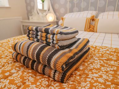 A stack of crocheted blankets on a patterned bedspread in a bedroom at The Store Rooms in Whitby