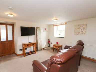 A living room with brown leather sofas wooden door and TV on the wall at Garreg Wen Isaf Bach in Penygroes near Caernarfon