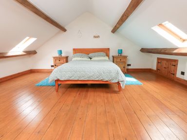 A bedroom with a bed between two nightstands under slanted ceilings with wooden beams at Garreg Wen Isaf Bach in Penygroes near Caernarfon