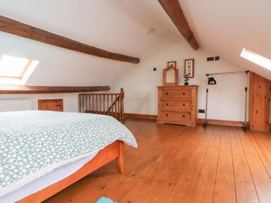 A bedroom with a wooden bed frame, dresser, and clothes rack under slanted ceilings with exposed wooden beams at Garreg Wen Isaf Bach in Penygroes near Caernarfon