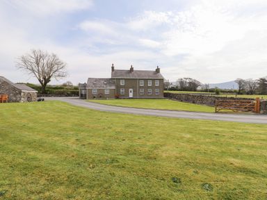 A two-story house with multiple windows and a chimney surrounded by a stone wall and a grassy lawn at Garreg Wen Isaf Bach in Penygroes near Caernarfon