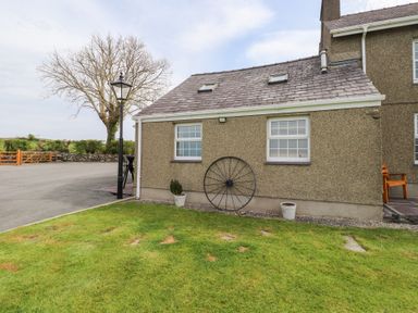 The exterior of a house with two windows a lamp post a tree two potted plants a large metal wheel and a wooden bench on a lawn at Garreg Wen Isaf Bach in Penygroes near Caernarfon