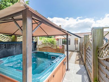 An outdoor hot tub with a canopy and wooden fencing beside a paved walkway at Willow Cottage in Ulrome near Skipsea