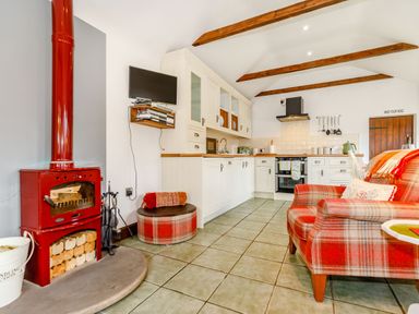 A kitchen with white cabinets red plaid armchair a red wood stove and a mounted television at Willow Cottage in Ulrome near Skipsea