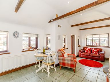 A living room with a small dining table and chairs and a red sofa at Willow Cottage in Ulrome near Skipsea