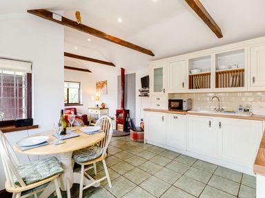 A kitchen and dining area with white cabinets wooden beams and a small dining table at Willow Cottage in Ulrome near Skipsea