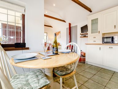 A kitchen dining area with a wooden table set for two with wine glasses and a bottle of wine at Willow Cottage in Ulrome near Skipsea