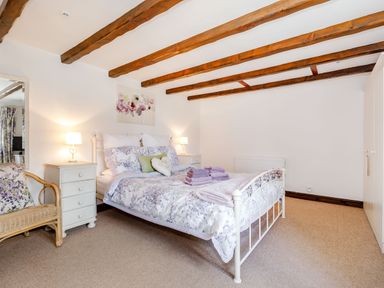 A bedroom with a bed with floral bedding two bedside tables with lamps a wicker chair and wooden ceiling beams at Willow Cottage in Ulrome near Skipsea