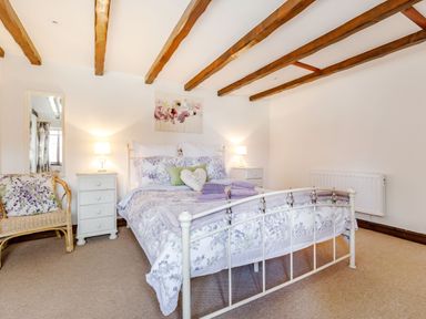 A bedroom with a floral bedspread on a metal bed frame and wooden ceiling beams at Willow Cottage Ulrome near Skipsea