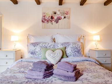 A bedroom with a double bed floral bedding and folded towels on the bed at Willow Cottage in Ulrome near Skipsea