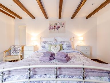 A bedroom with a bed and purple towels on it wooden beams on the ceiling and bedside tables with lamps at Willow Cottage in Ulrome near Skipsea