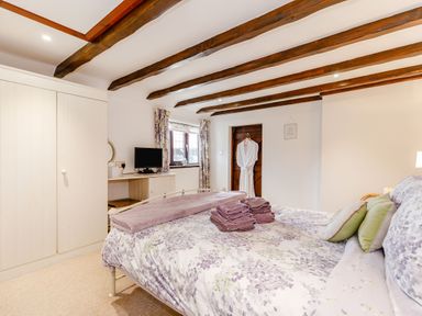 A bedroom with a floral bedspread wooden ceiling beams wardrobe and a small tv at Willow Cottage in Ulrome near Skipsea