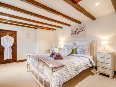 A bedroom with a double bed covered in floral bedding two bedside tables with lamps a wooden door with white robes hanging on it and wooden ceiling beams at Willow Cottage Ulrome near Skipsea