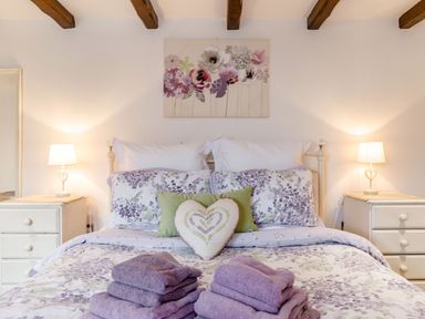 A bedroom with a bed dressed in floral bedding with folded towels and bedside tables with lamps at Willow Cottage in Ulrome near Skipsea