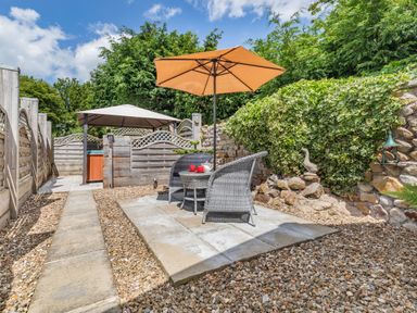 An outdoor patio with two wicker chairs and a table under an orange umbrella next to a stone wall and greenery at Willow Cottage in Ulrome near Skipsea