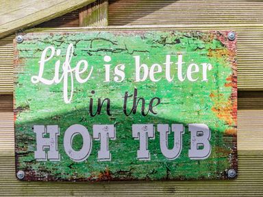 A weathered green sign with the words Life is better in the hot tub on a wooden surface at Willow Cottage in Ulrome near Skipsea