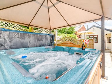 An outdoor hot tub with bubbles under a canopy with a bottle and glass beside it at Willow Cottage in Ulrome near Skipsea