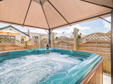 An outdoor hot tub with bubbling water under a canopy with wooden fencing and houses in the background at Willow Cottage in Ulrome near Skipsea