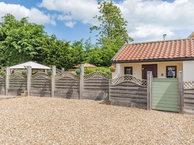 A gravel yard with a wooden fence and a small building with a tiled roof at Willow Cottage in Ulrome near Skipsea