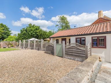 An exterior view of a single story house with a tiled roof a gravel driveway wooden fences and greenery at Willow Cottage in Ulrome near Skipsea