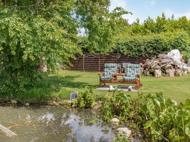 A garden with a pond two chairs and a wooden fence at Willow Cottage in Ulrome near Skipsea