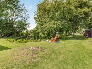 A garden with two wooden chairs on a stone slab near a pond surrounded by trees and grass at Willow Cottage Ulrome near Skipsea