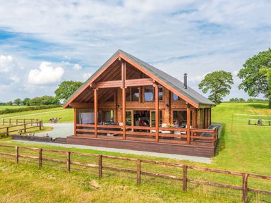 A wooden cabin with large windows and a deck in a grassy field at Hampton Lodge in Ellesmere