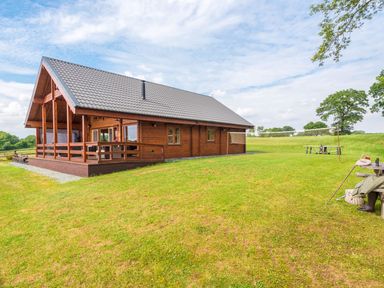 A wooden house with a covered porch and a badminton net on a grass lawn at Hampton Lodge in Ellesmere