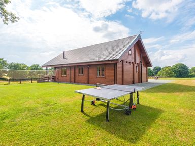 A wooden cabin with a tiled roof and a ping pong table on a grass lawn at Hampton Lodge in Ellesmere