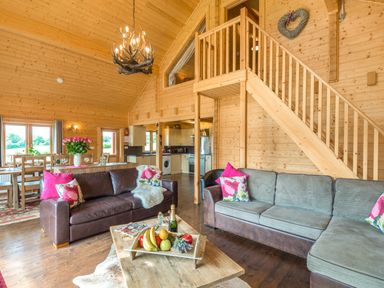 A living room with two sofas a wooden coffee table and a dining area in a wooden cabin at Hampton Lodge in Ellesmere