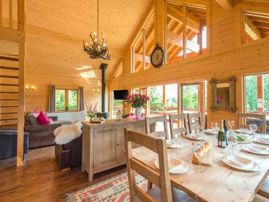 A dining area with a wooden table set for a meal and a living room with sofas and a wood stove in a wooden cabin at Hampton Lodge in Ellesmere