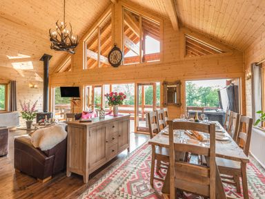An open plan wooden dining and living room with a dining table set for a meal and a leather sofa at Hampton Lodge in Ellesmere