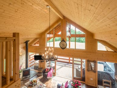 An open wooden living room with a chandelier wood stove and large windows at Hampton Lodge in Ellesmere
