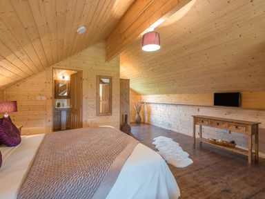 A bedroom with wooden walls and ceiling a bed with a blanket and pillows a wooden console table and a mounted television at Hampton Lodge in Ellesmere