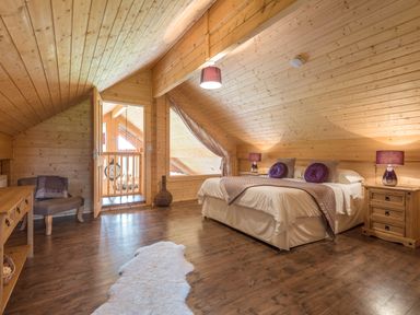 A bedroom with a large bed and two bedside tables with lamps in a wooden cabin at Hampton Lodge in Ellesmere