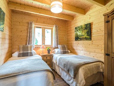 A wooden bedroom with two single beds a nightstand with a lamp and flowers and a wardrobe at Hampton Lodge in Ellesmere
