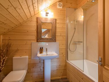 A bathroom with wooden walls a toilet sink mirror and bathtub with shower at Hampton Lodge in Ellesmere